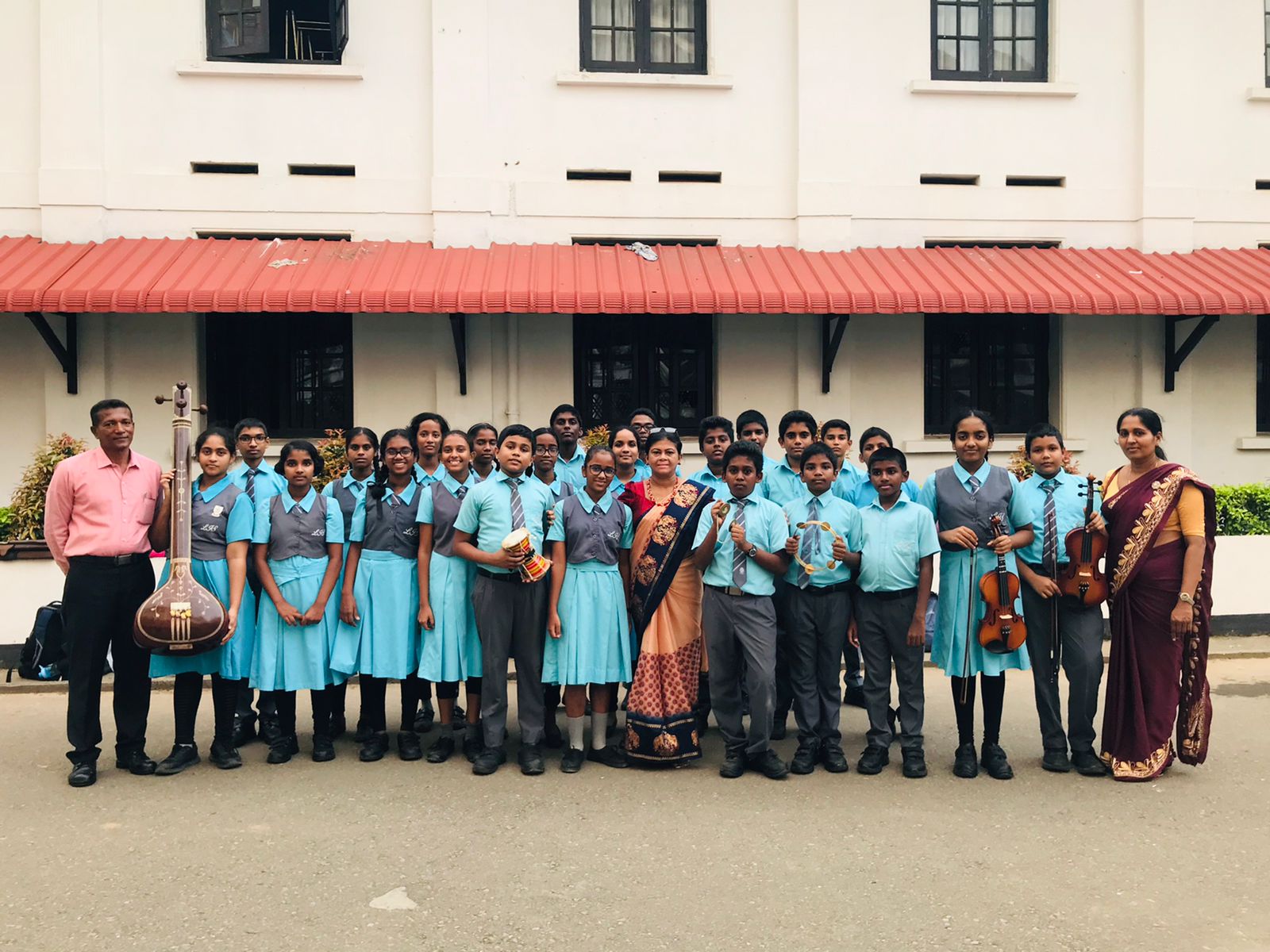 School band group photo with proud teachers in front of their school.