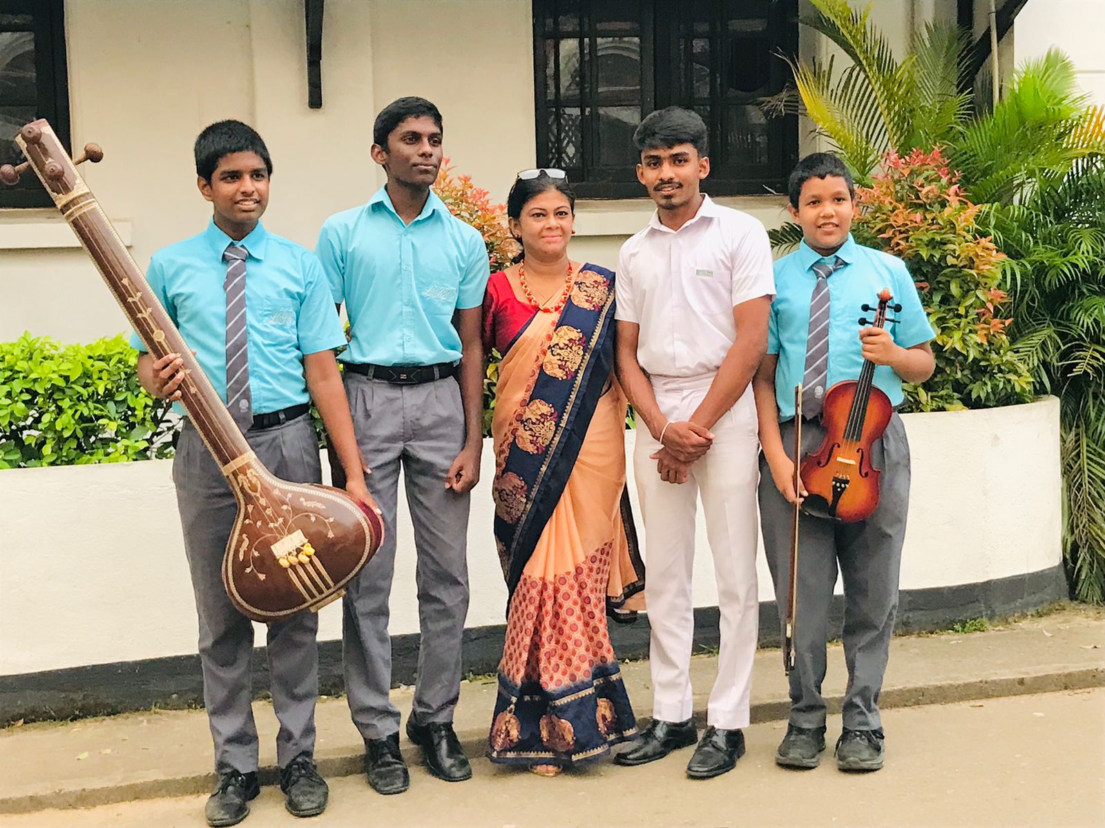 Family and musicians posing outdoors with sitar and violin.