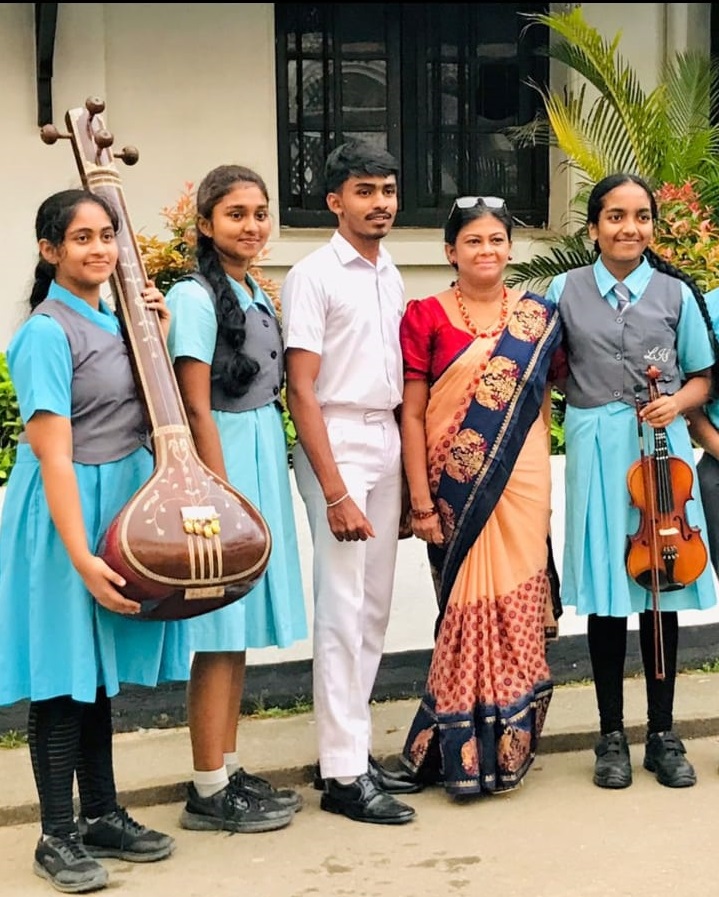 Students and teacher posing with musical instruments outside school building.