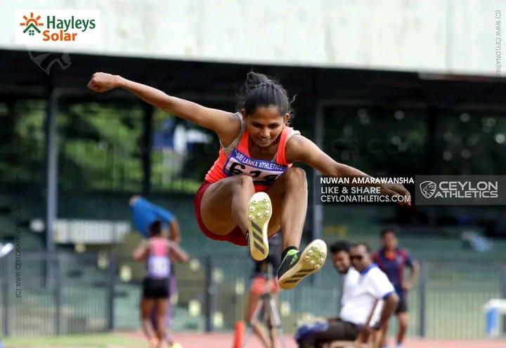 Female athlete mid-air during long jump at outdoor stadium event, sponsored by Hayleys Solar and Ceylon Athletics.