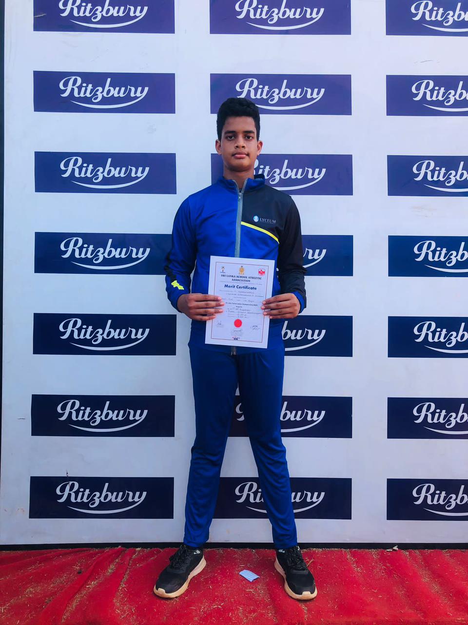 Young athlete holding a certificate in front of a Ritzbury backdrop on a red carpet.