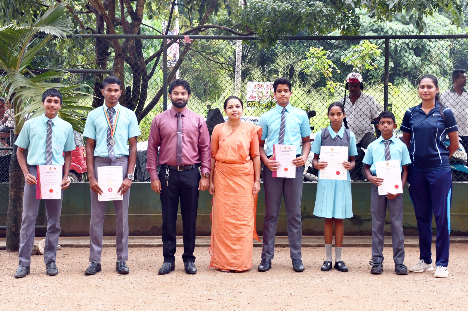 Students and teachers at outdoor school award ceremony holding certificates.