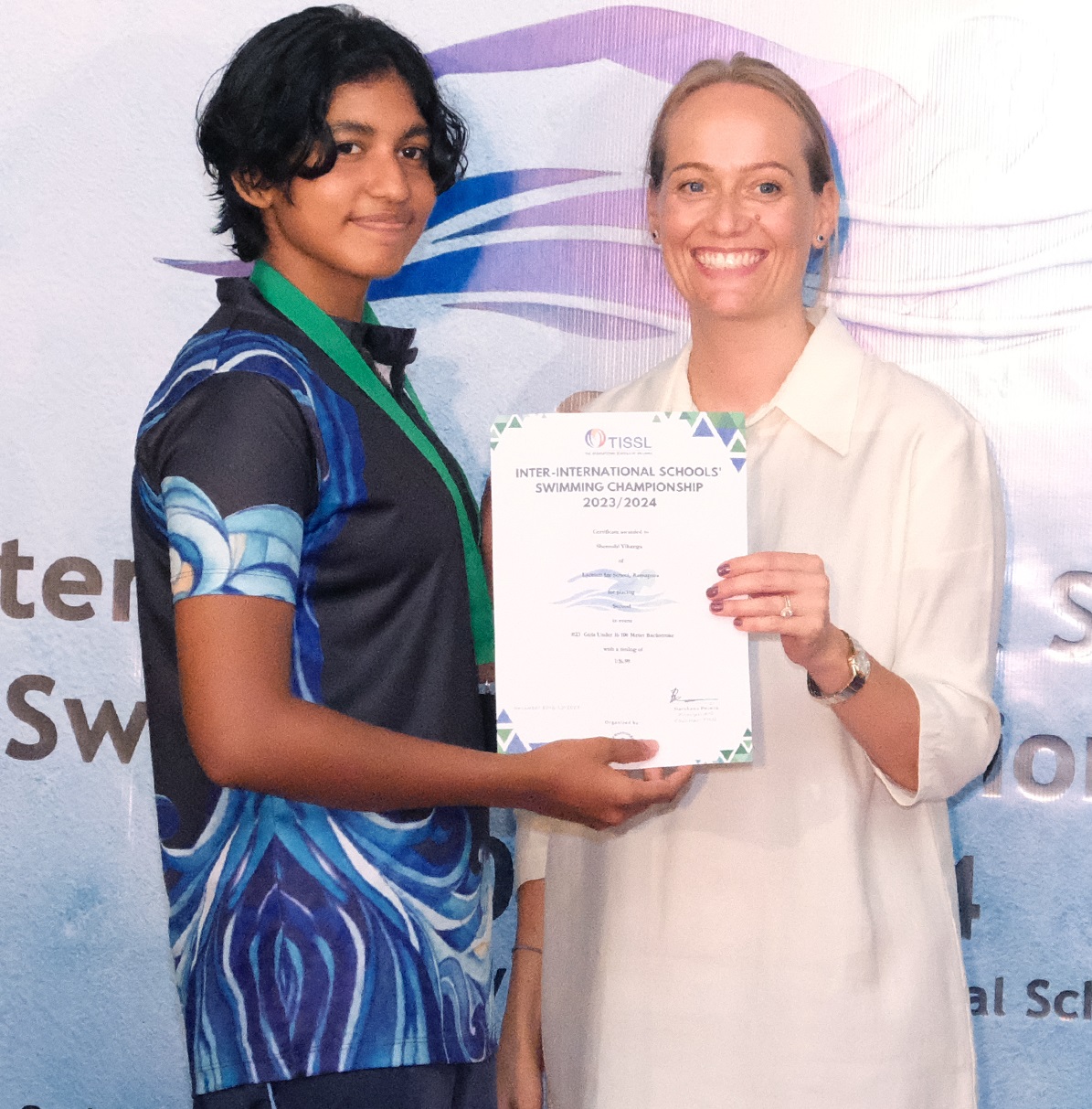 Two people smiling, presenting a swimming award certificate at an international school event.