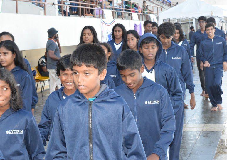 Students marching in blue uniforms at school event, spectators in background.