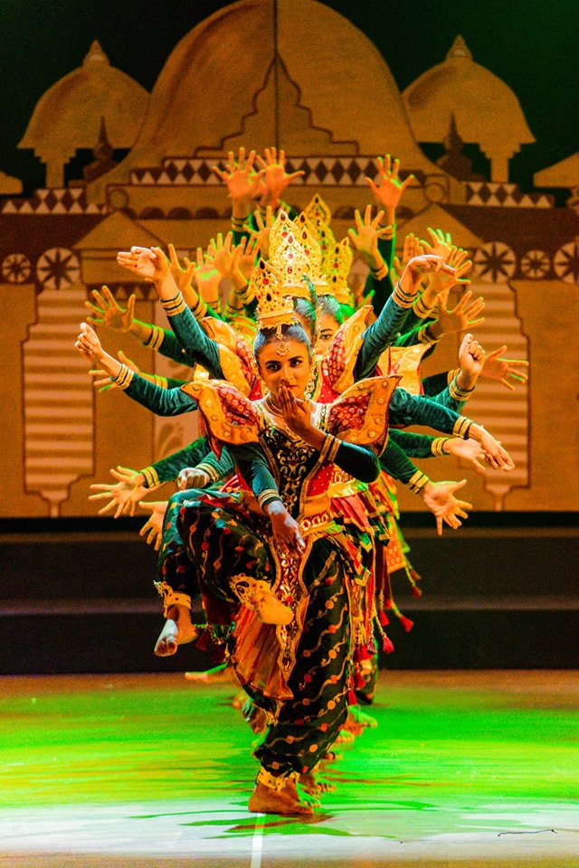 Traditional dancers in colorful costumes with multi-arm formation on stage.