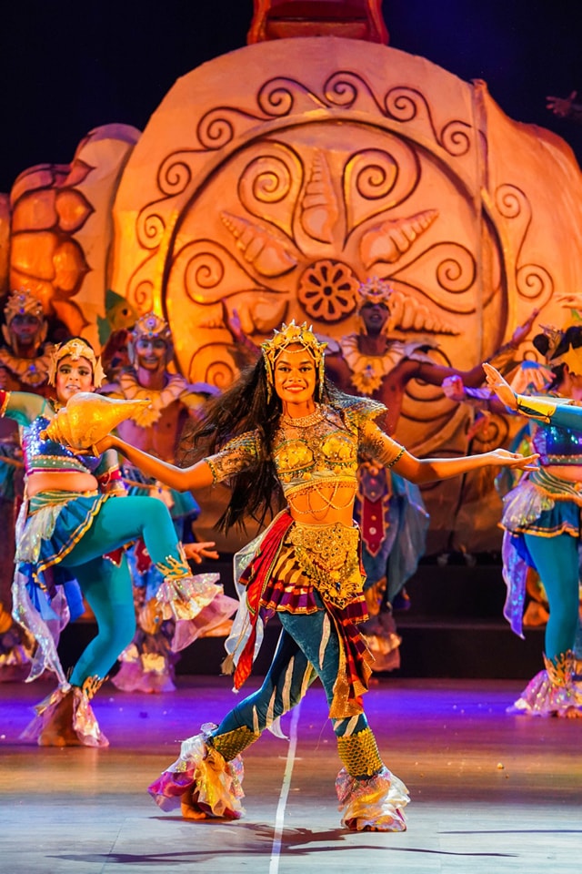 Energetic cultural dance on ornate stage with vibrant costumes and joyful expressions.