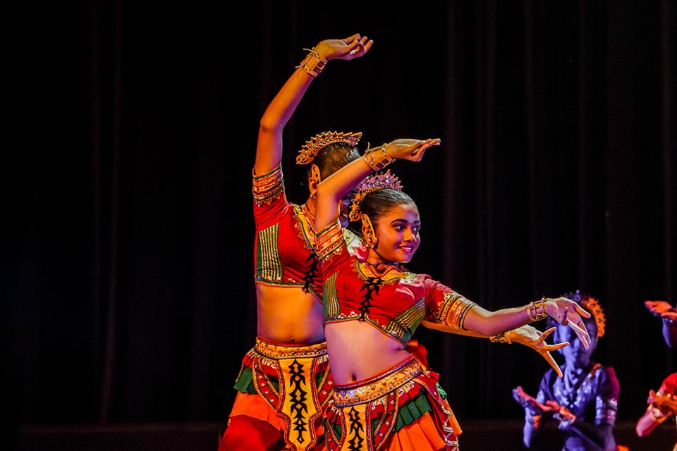Two dancers in vibrant traditional costumes perform a culturally rich dance on stage.