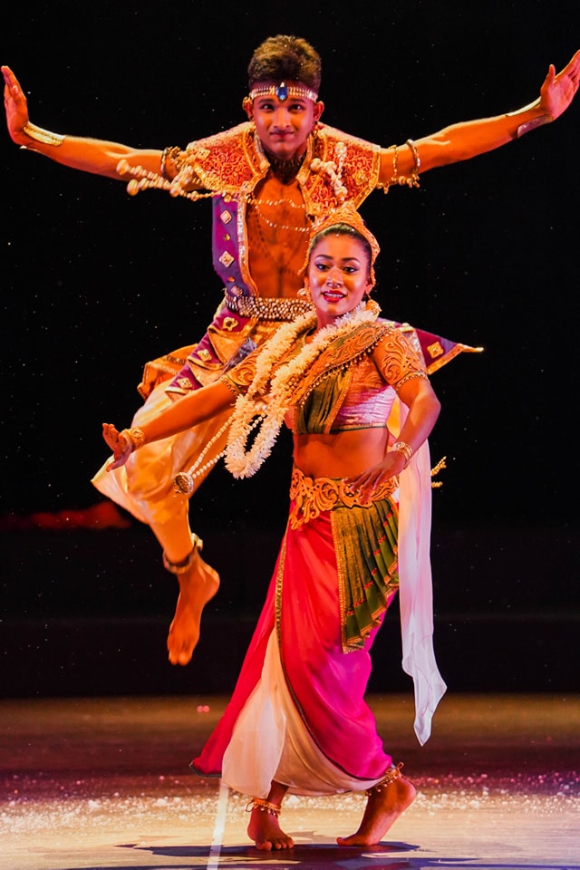Traditional dancers in vibrant costumes, mid-performance, against a dark background.