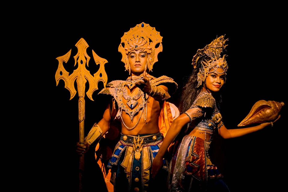 Two mythical figures in ornate costumes: one with a trident, one with a conch shell.