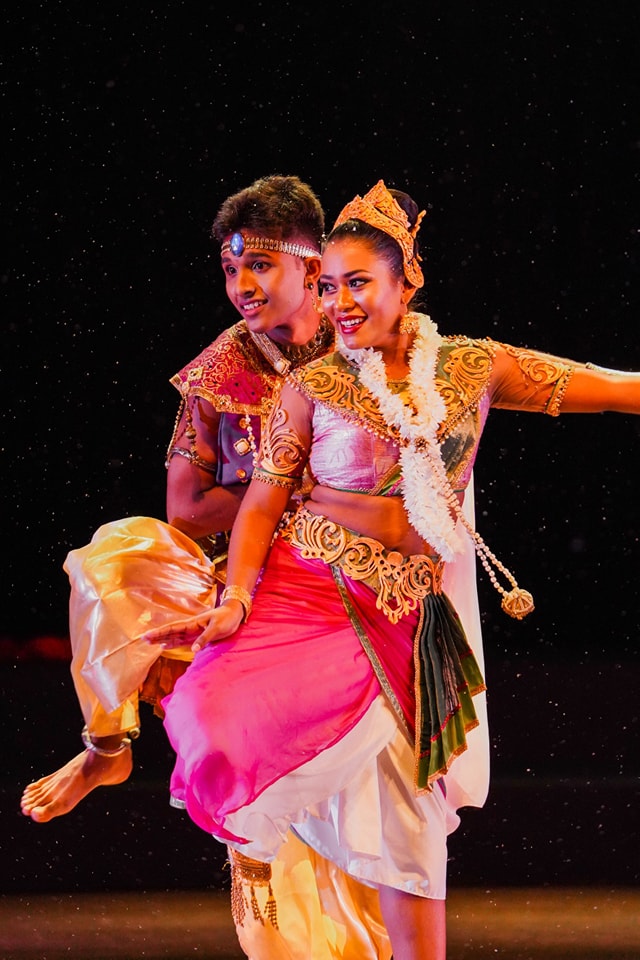 Traditional South Asian dancers in colorful attire performing energetically on a dark stage.