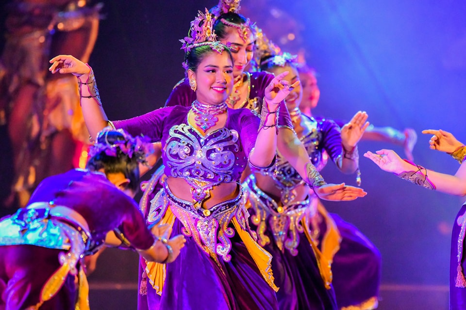 Traditional dancers in vibrant costumes perform under colorful stage lights.
