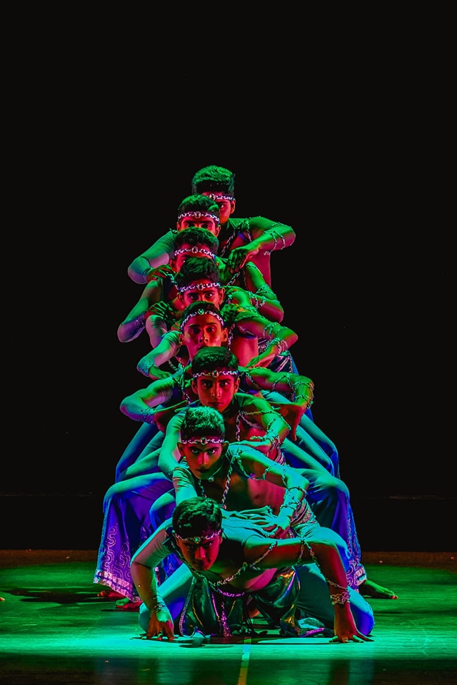 Vibrant traditional dancers in colorful costumes perform synchronized moves on a dramatically lit stage.
