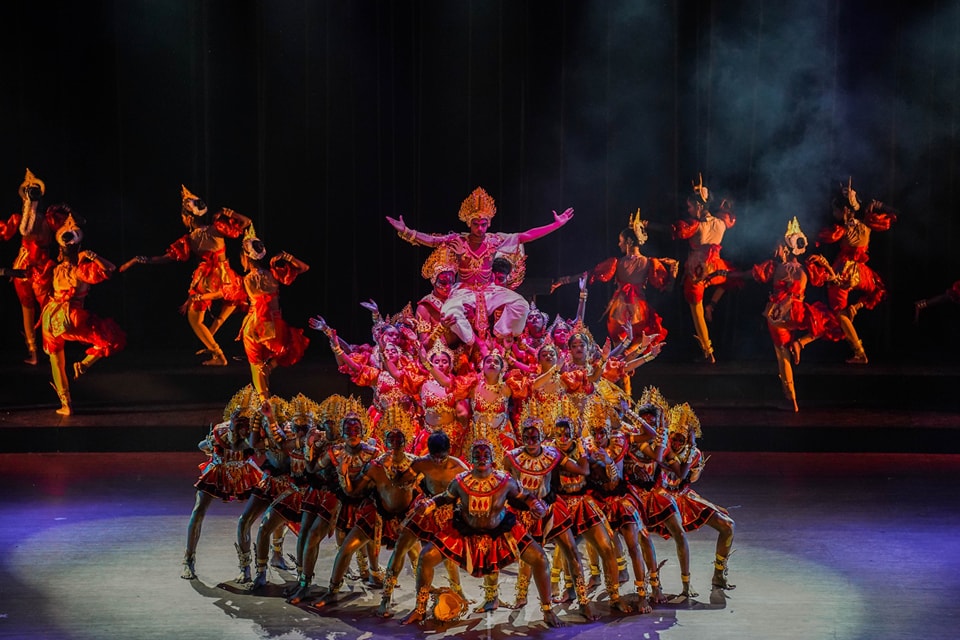 Cultural dance performance with vibrant costumes and dynamic poses on a brightly lit stage.
