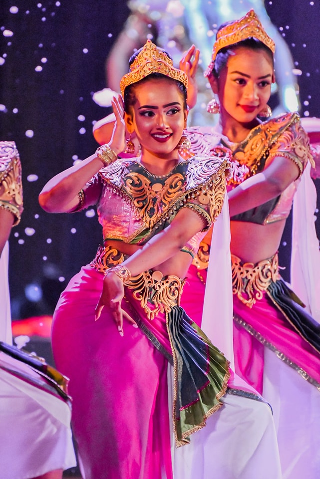 Two women in vibrant traditional costumes performing a synchronized cultural dance.