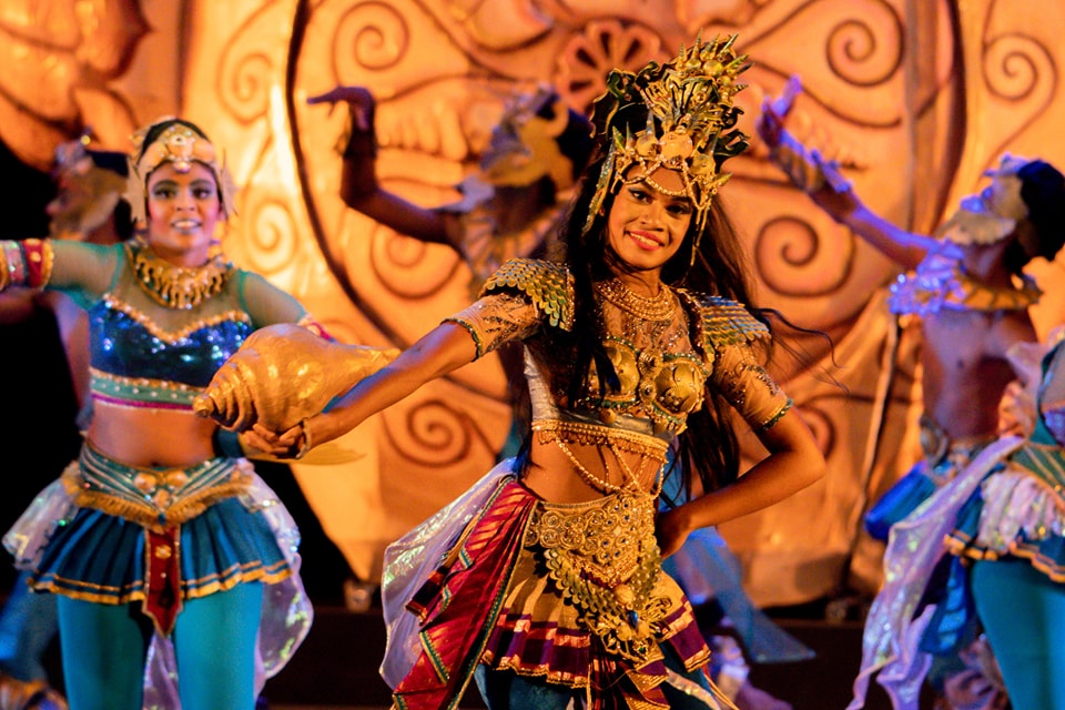 Traditional Indian dance with vibrant costumes and conch shell prop on ornate stage.