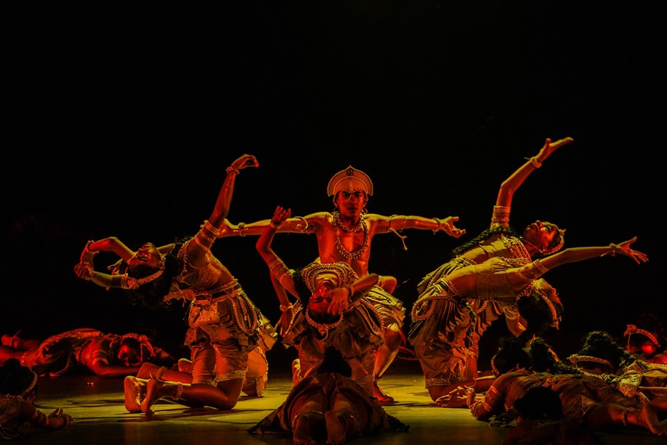 Dynamic traditional dance performance with elaborate costumes under dramatic, warm lighting.