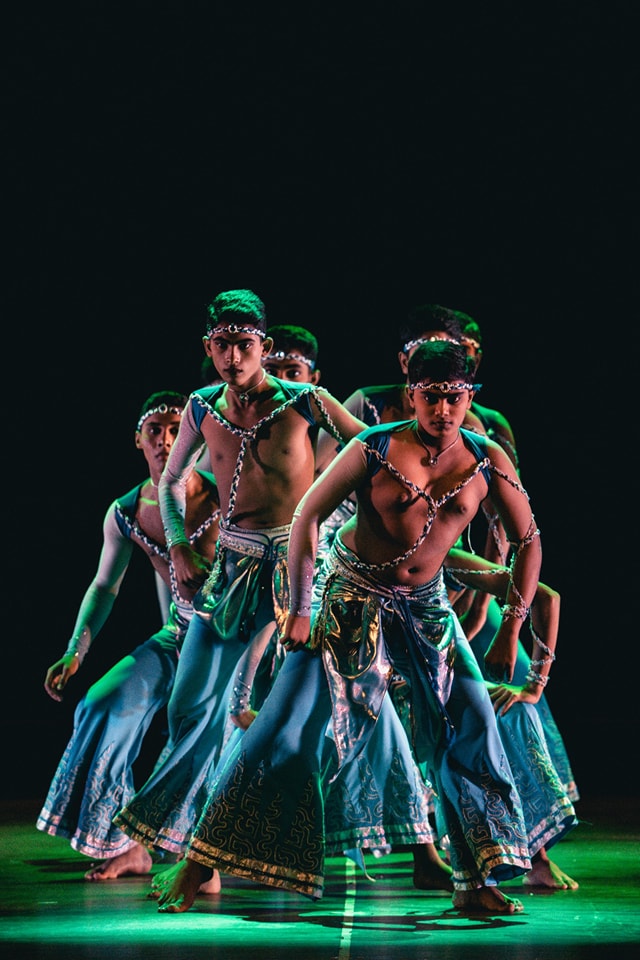 Traditional dancers in vibrant blue costumes performing on a dramatically lit stage.