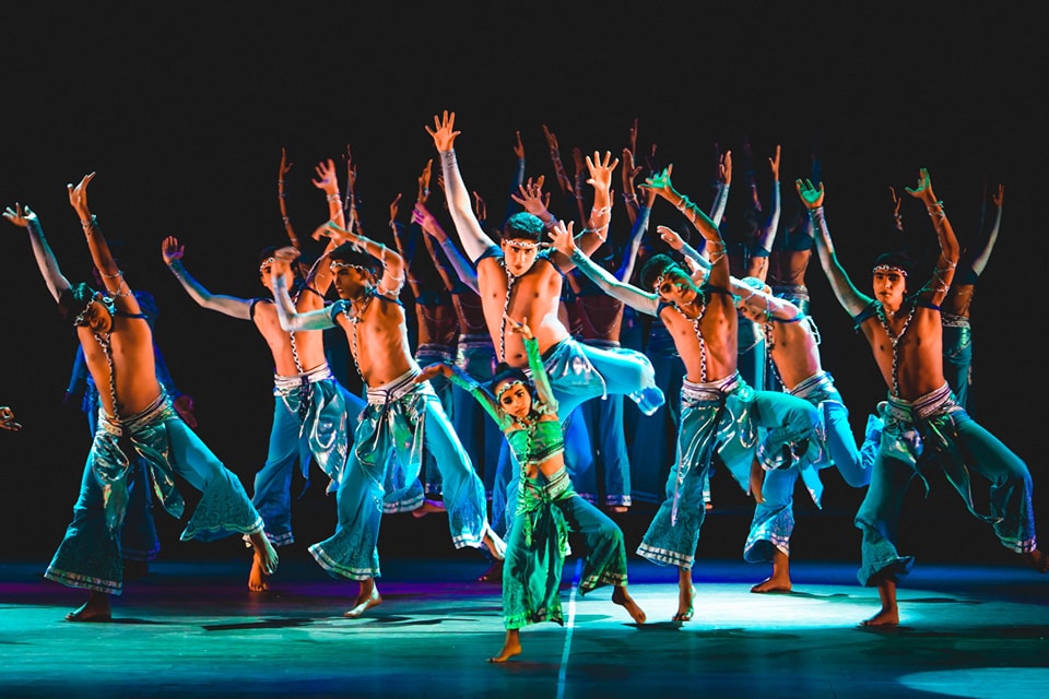 Dancers in colorful costumes performing a lively and coordinated cultural dance on stage.