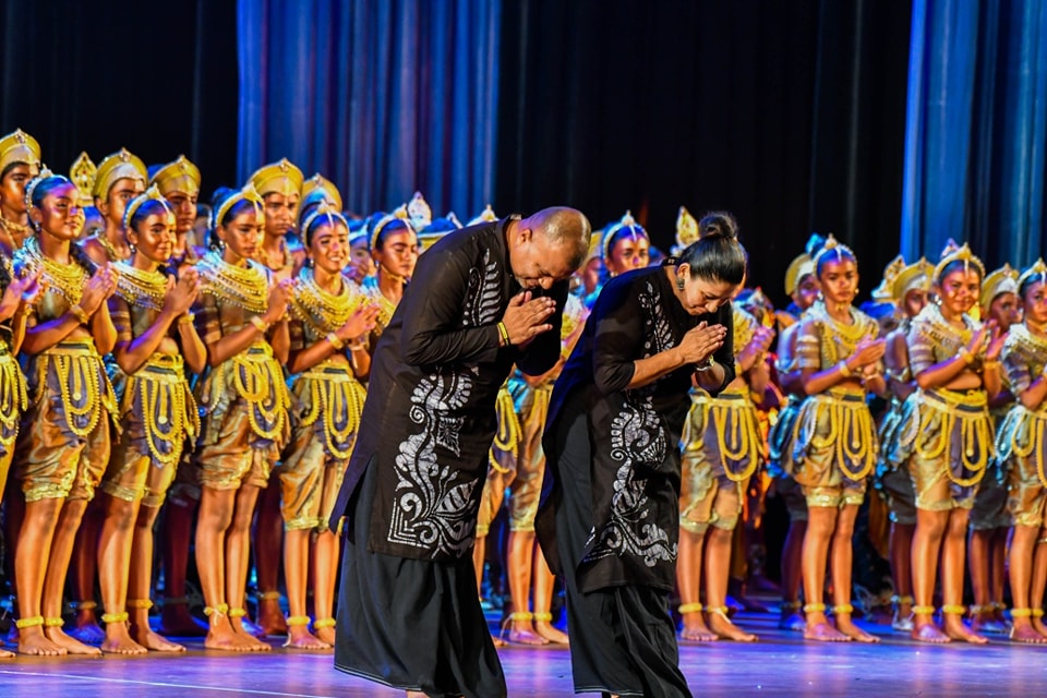 Final bow of cultural dancers in elegant costumes under vibrant stage lighting.