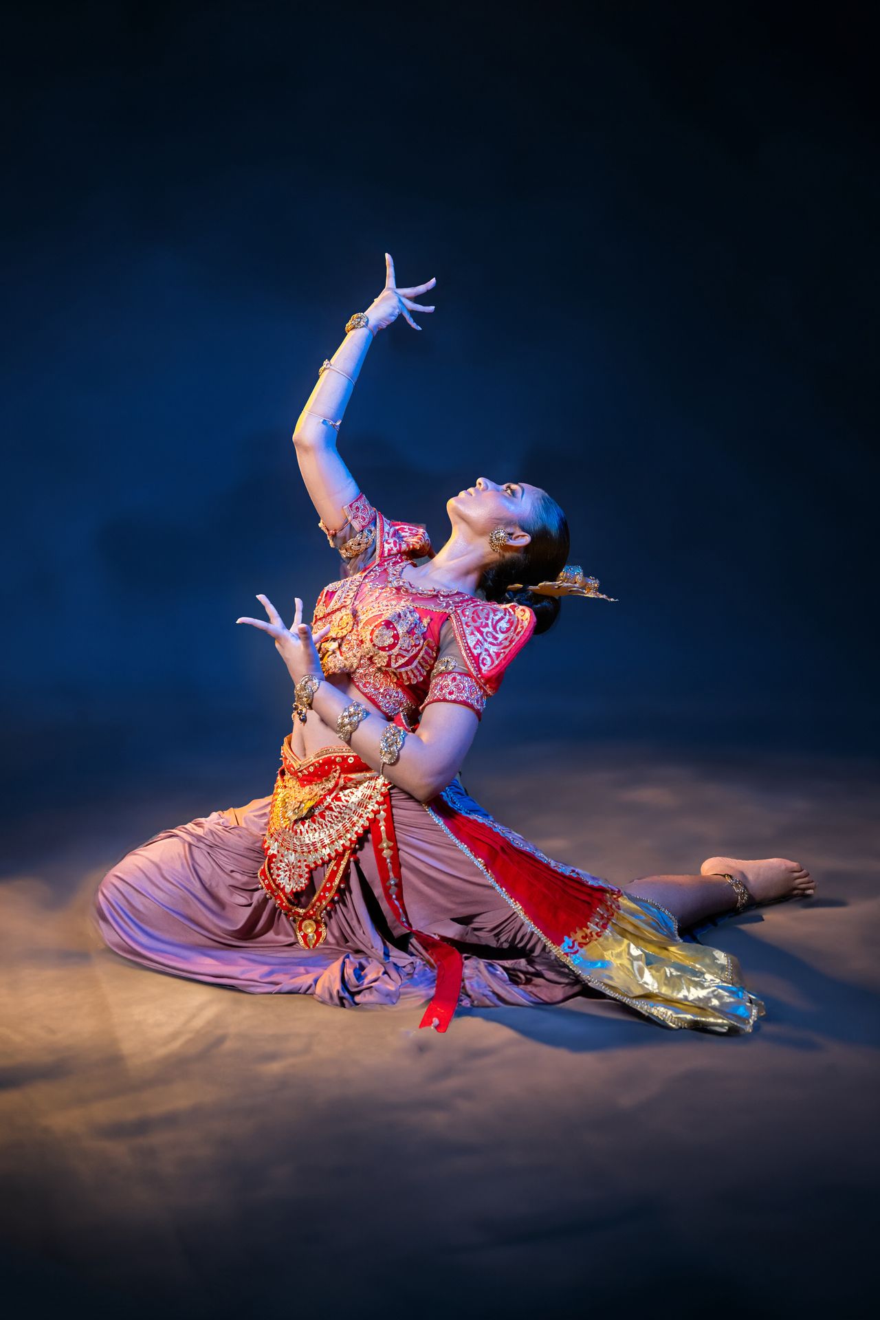 A dancer in vibrant traditional attire strikes a dramatic pose on stage.