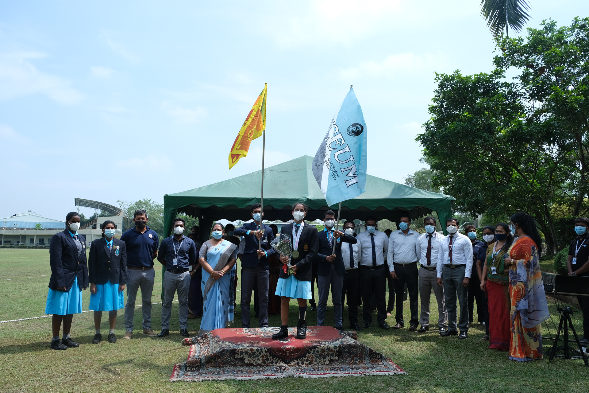 Formal outdoor award ceremony with students and adults in masks, holding a trophy.
