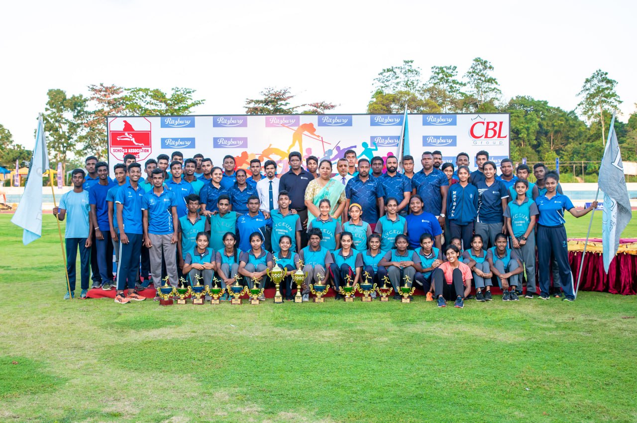 Sports team celebrating with trophies on a grassy field, festive banner in background.