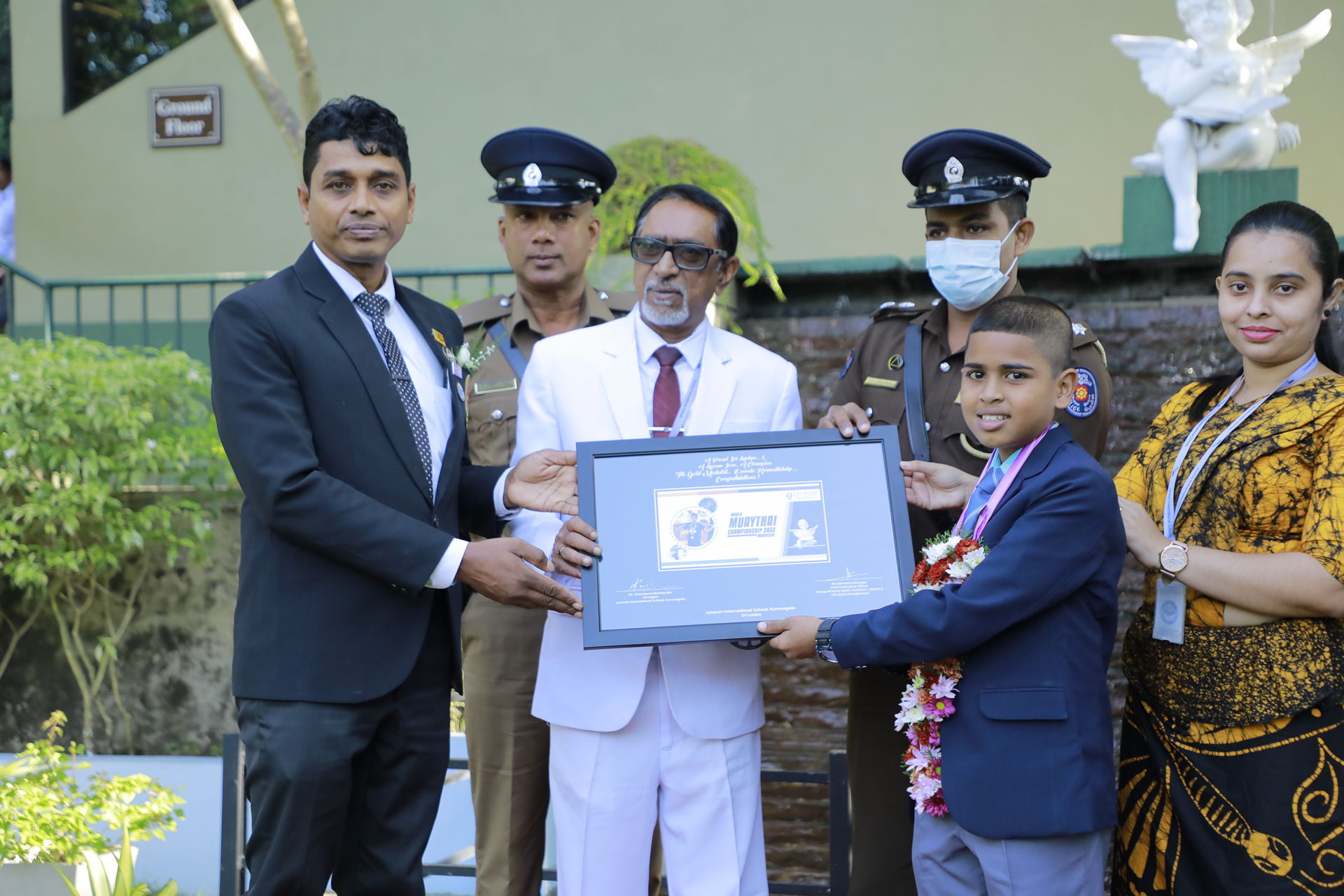 Outdoor award ceremony with uniformed officers presenting a framed certificate to a young boy.