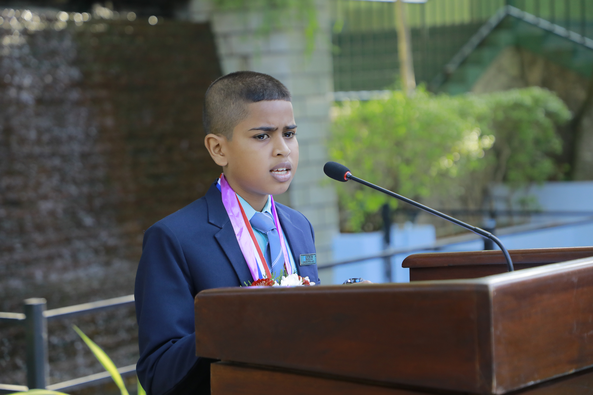 Young boy in suit delivering speech at outdoor formal event.