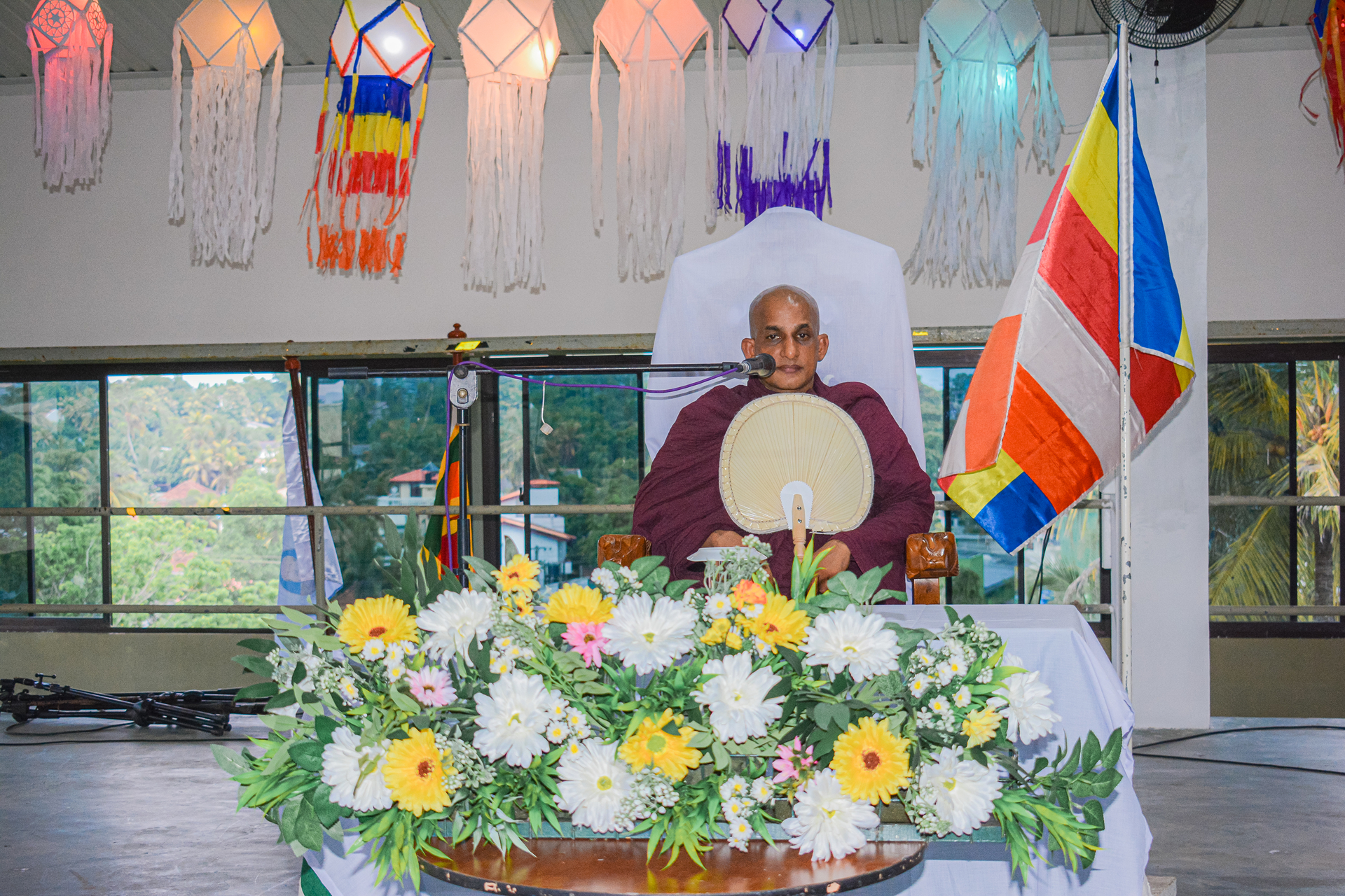 Buddhist monk in ceremony with flowers, colorful flags, and natural light.