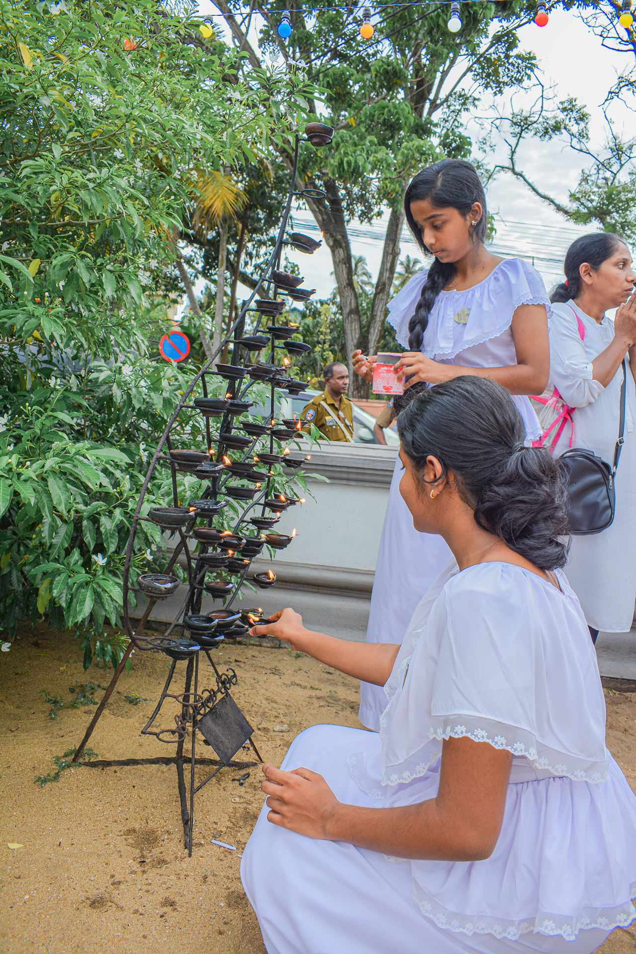 Women performing sacred oil lamp ritual in lush outdoor setting.