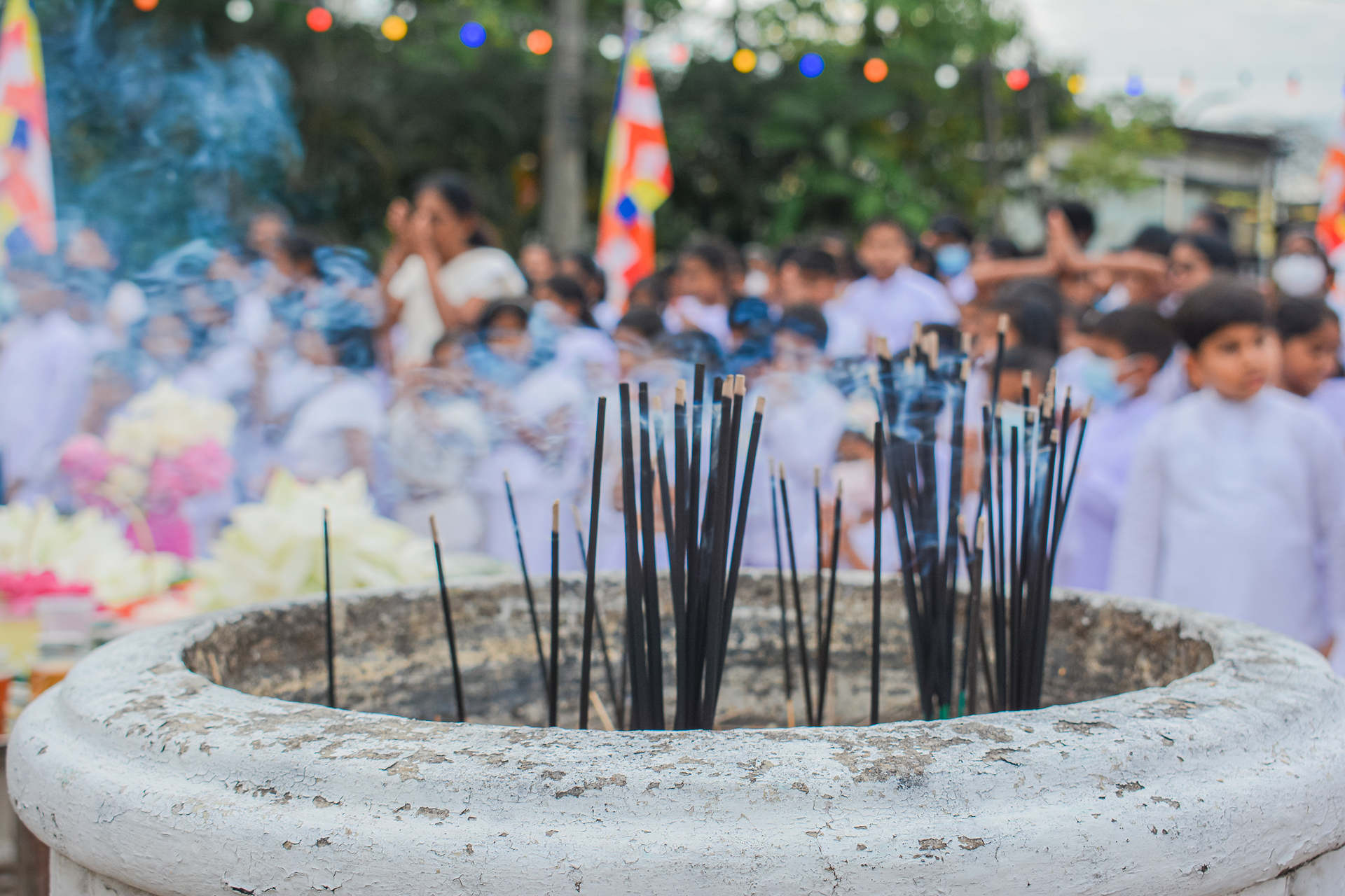 Incense burner amidst a crowd in white attire with colorful flags and festive lights.
