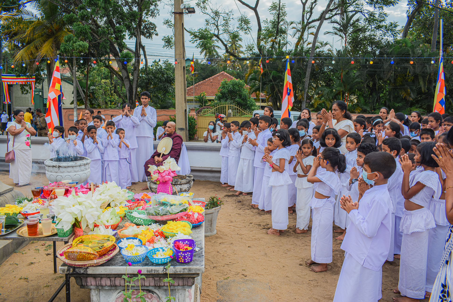 Childrens outdoor prayer ceremony with colorful offerings and traditional flags.
