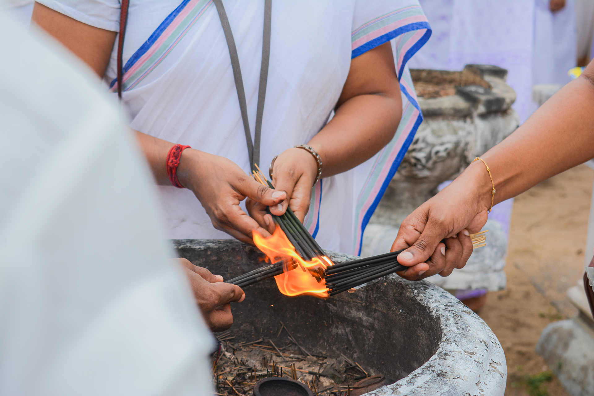 Participants lighting incense sticks from a central fire during a traditional ceremony.