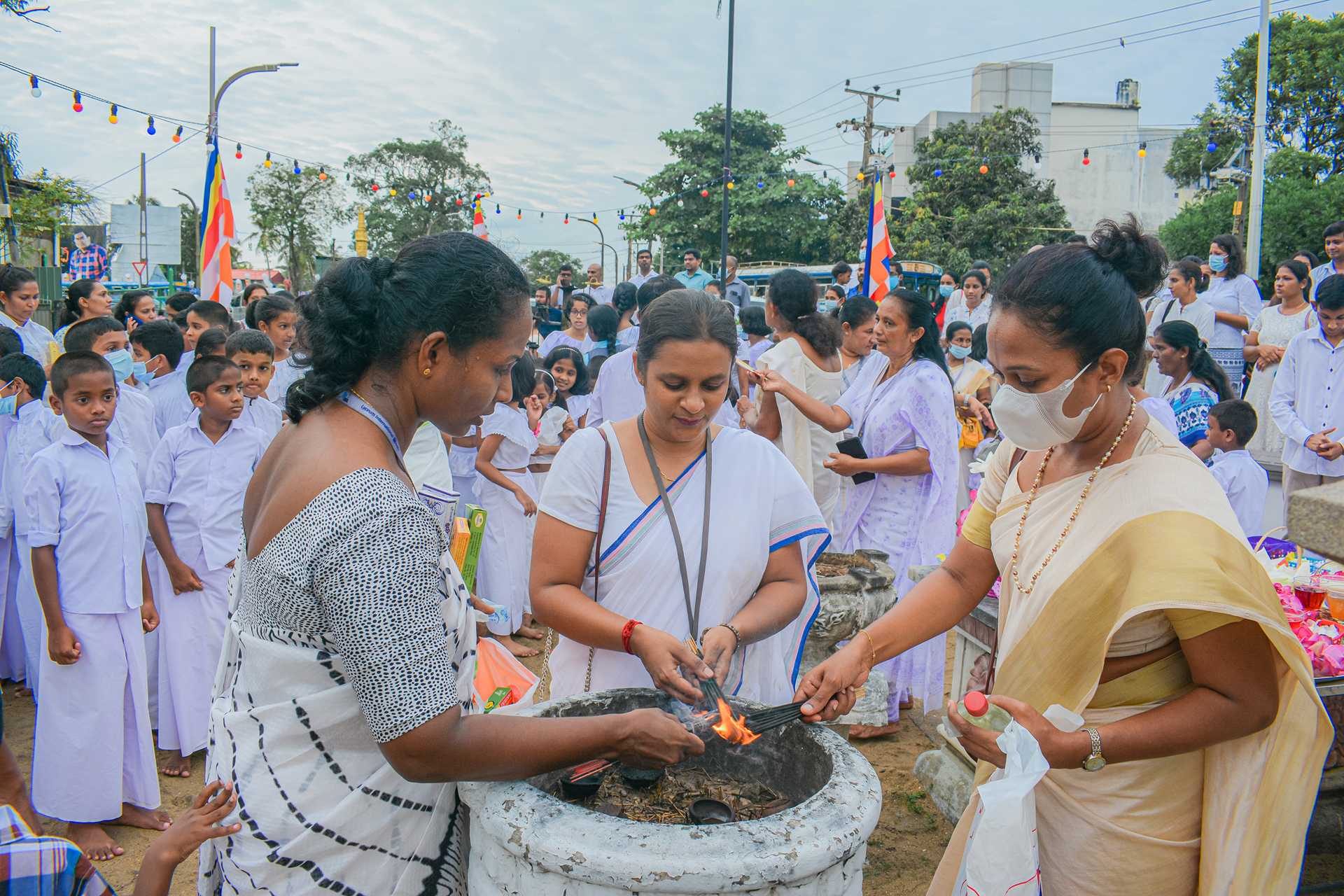 Community members in traditional attire participate in a ceremonial fire lighting outdoors.