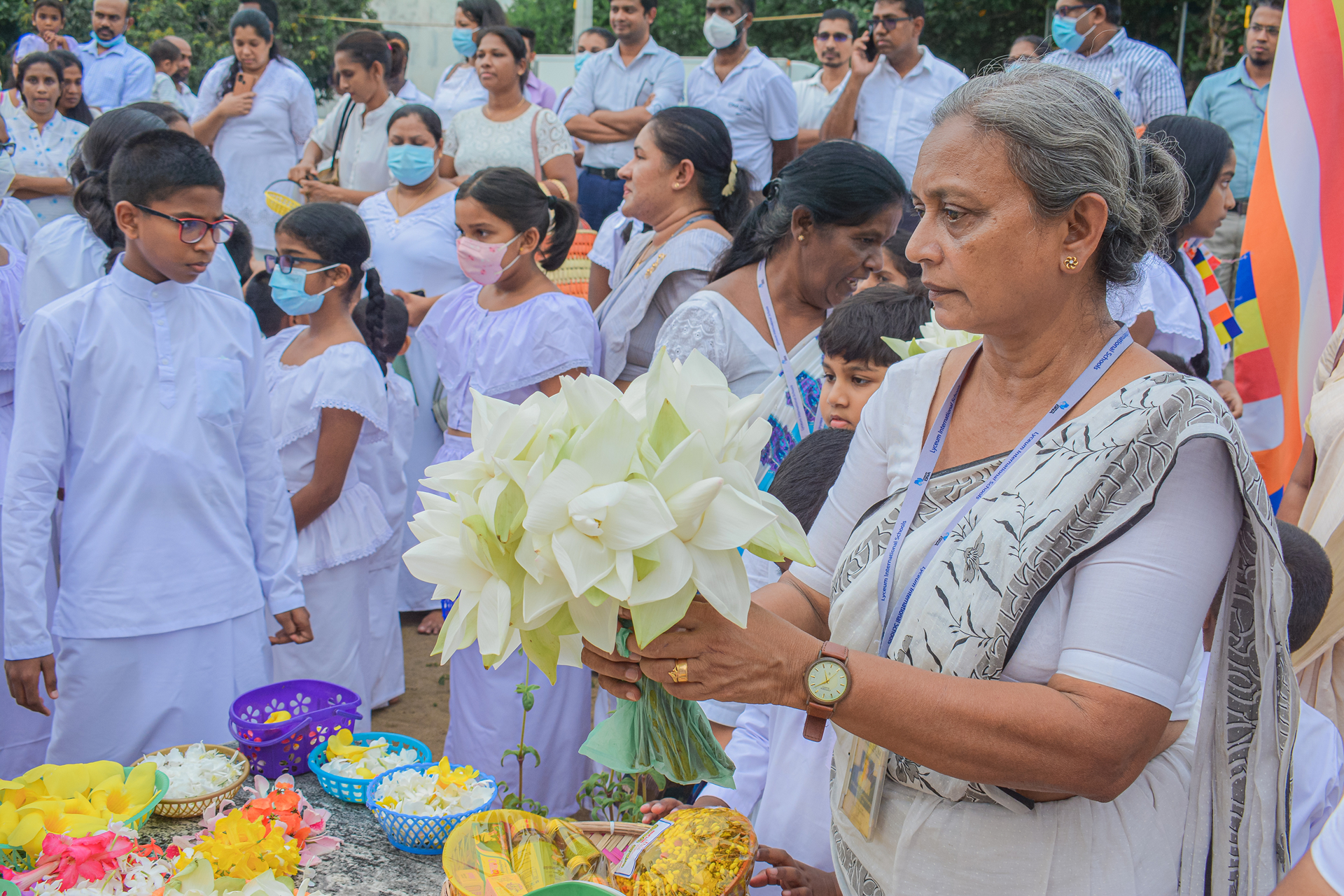 Elderly woman leading a floral ceremony with children and adults in white attire.