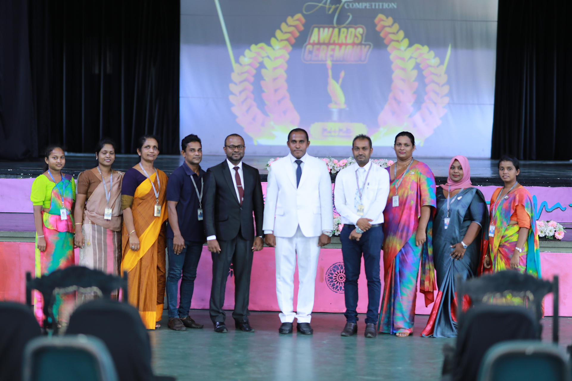 Nine formally dressed individuals posing on stage at an awards ceremony.