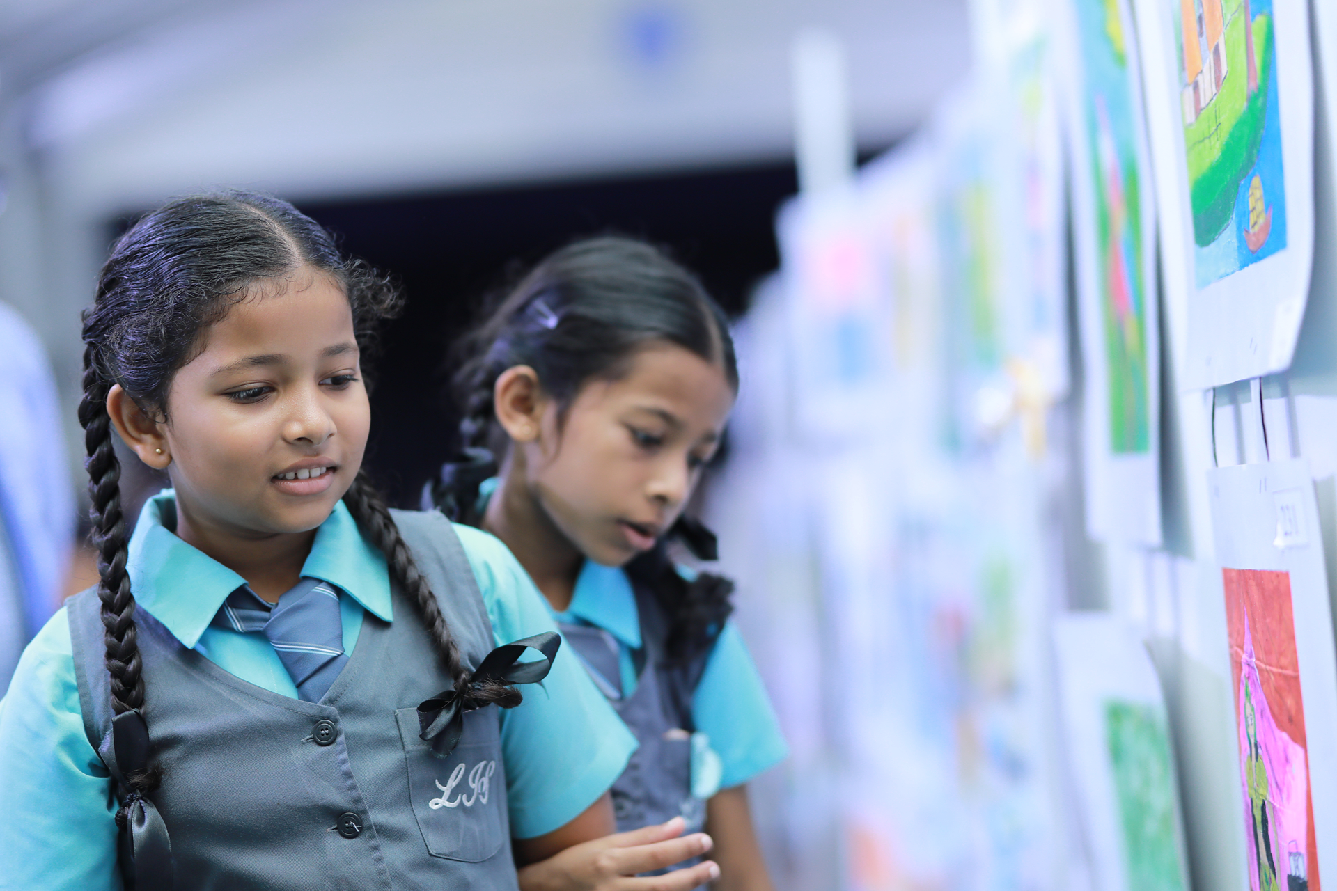 Schoolgirls in uniforms admiring colorful artwork at a school exhibition.