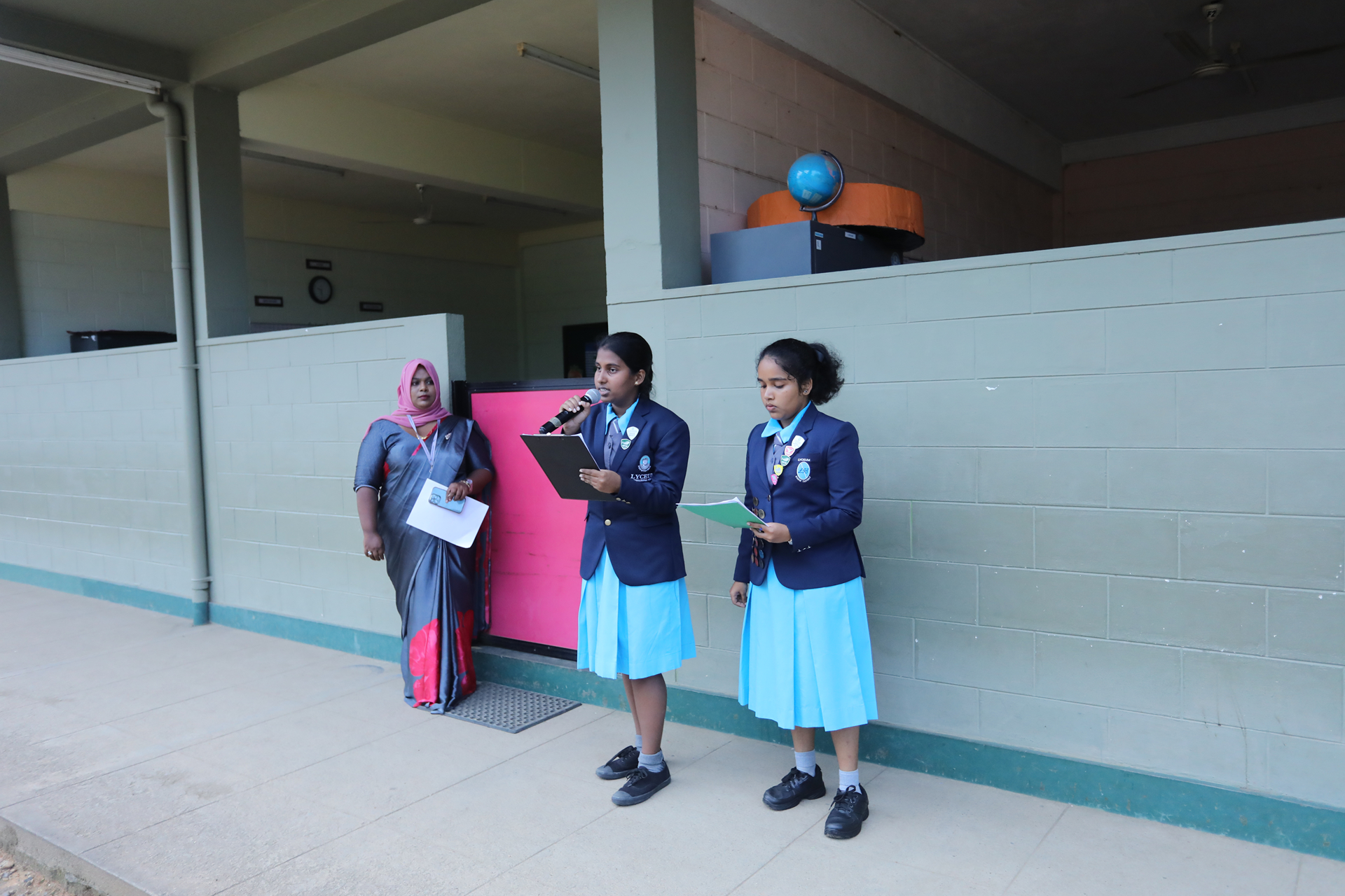 Schoolgirls presenting with teacher in vibrant saree supervising.