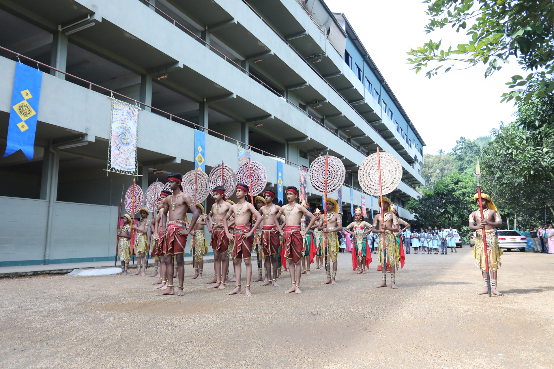 Traditional festival procession with men in ceremonial attire in front of a modern building.