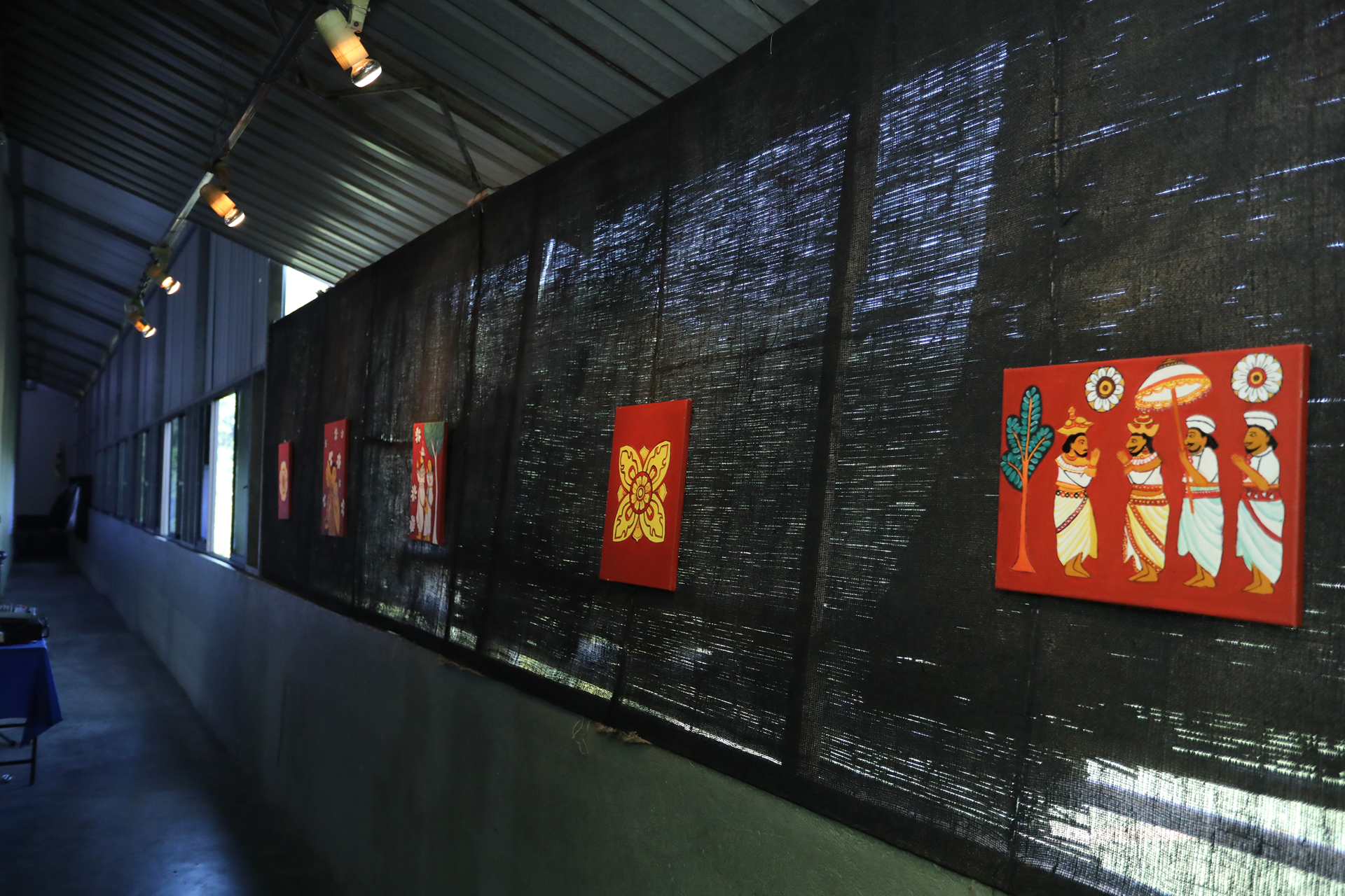 Contemporary art corridor with vibrant red paintings illuminated by spotlights on a dark wall.