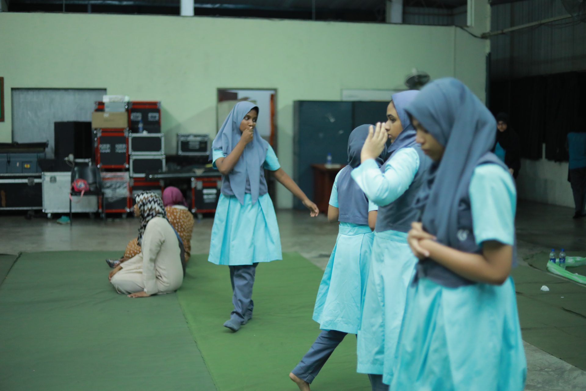 Girls in blue uniforms chatting on green mats in a community room.
