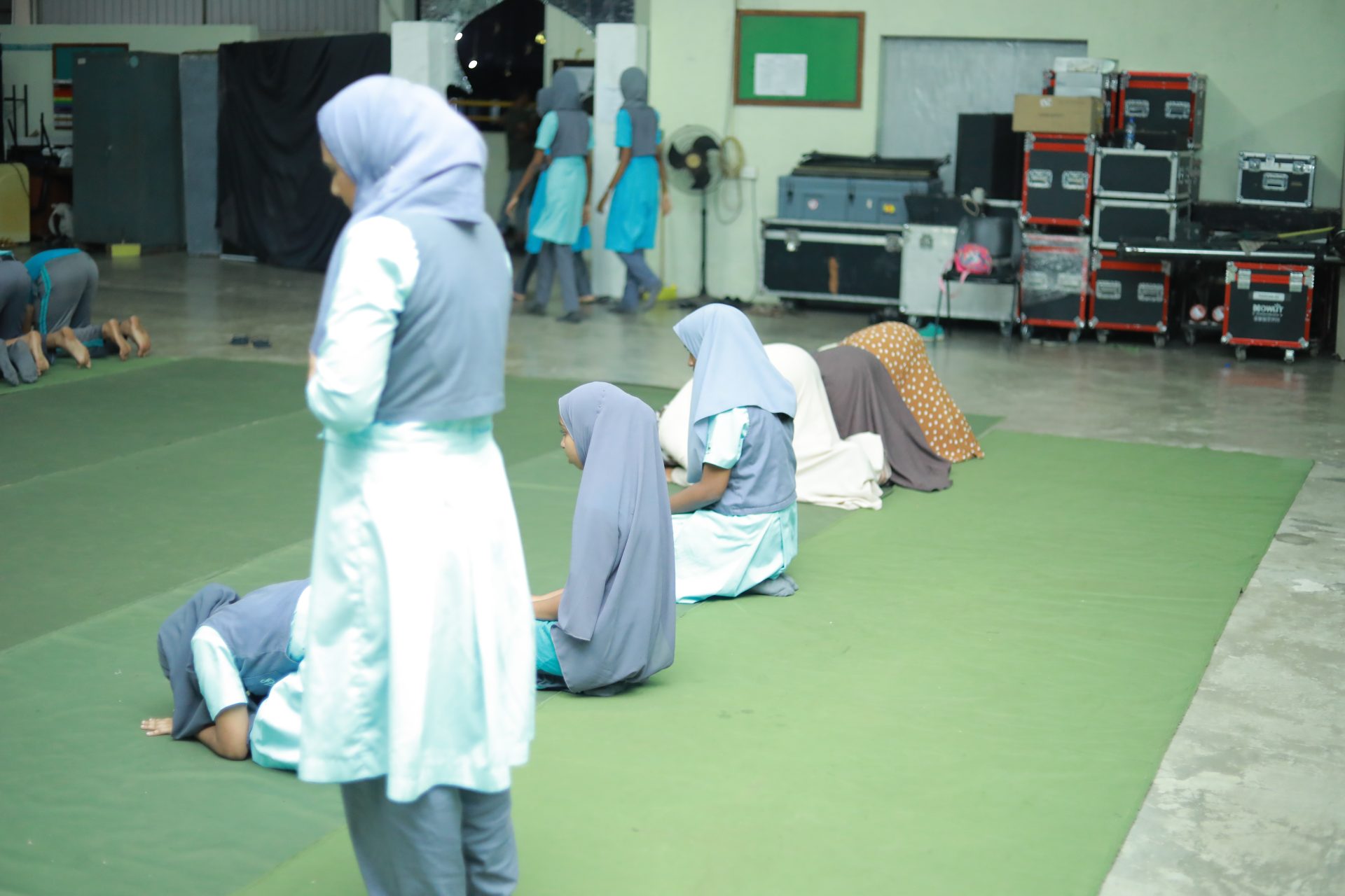 Women praying on a green mat in a multipurpose room.