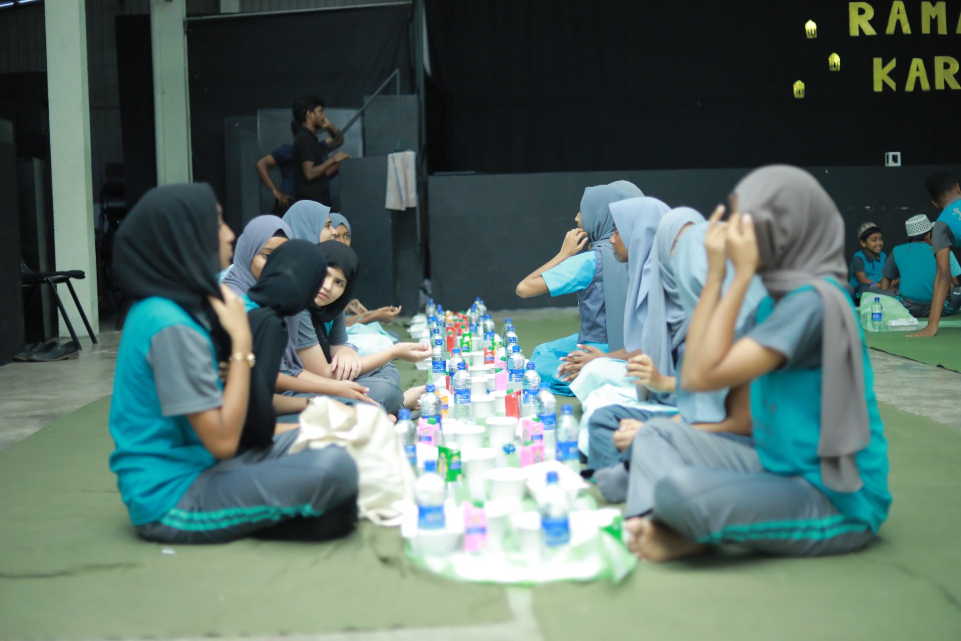 Young girls in headscarves enjoy a communal meal during a Ramadan celebration.