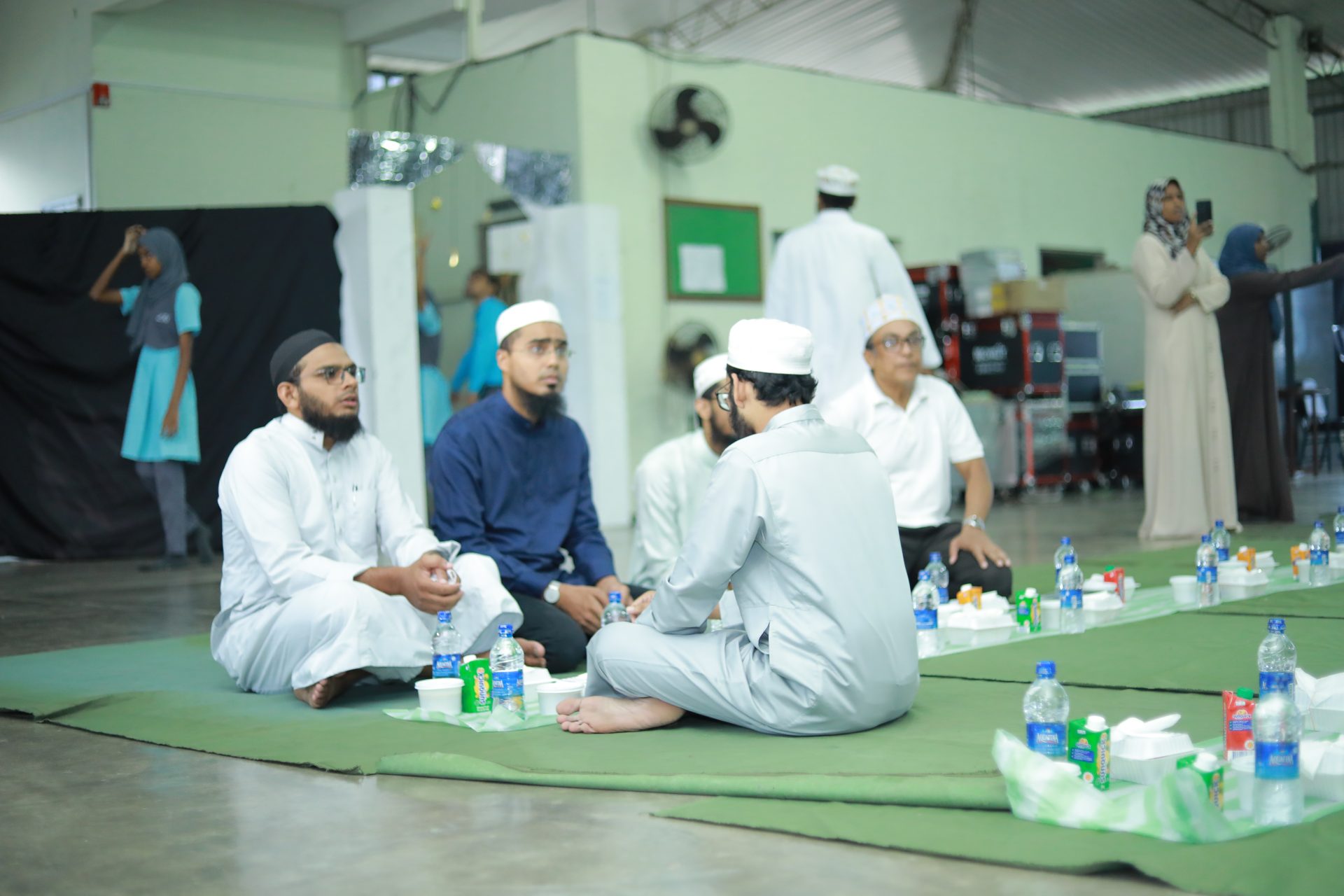 Group of people sharing a meal and conversations in a hall.