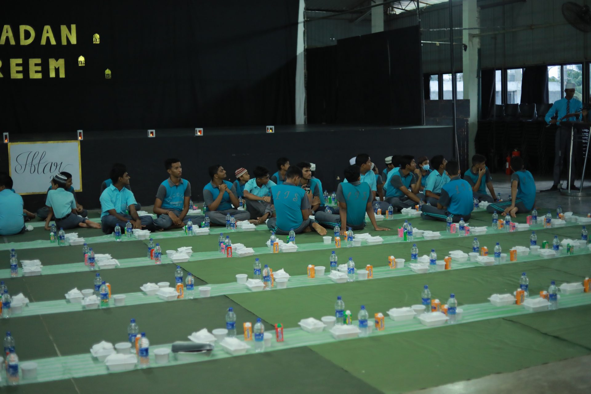 Community iftar event with children in blue shirts, food, and Ramadan Kareem banner.