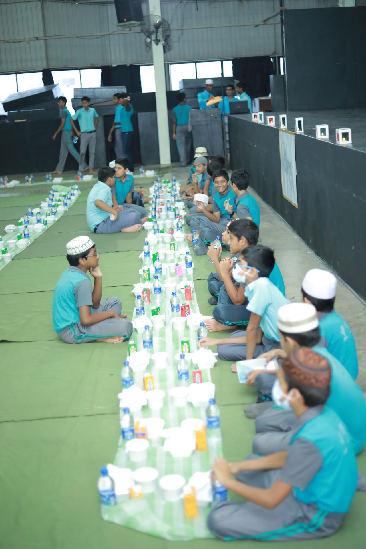 Children in matching outfits enjoying a supervised communal snack indoors.