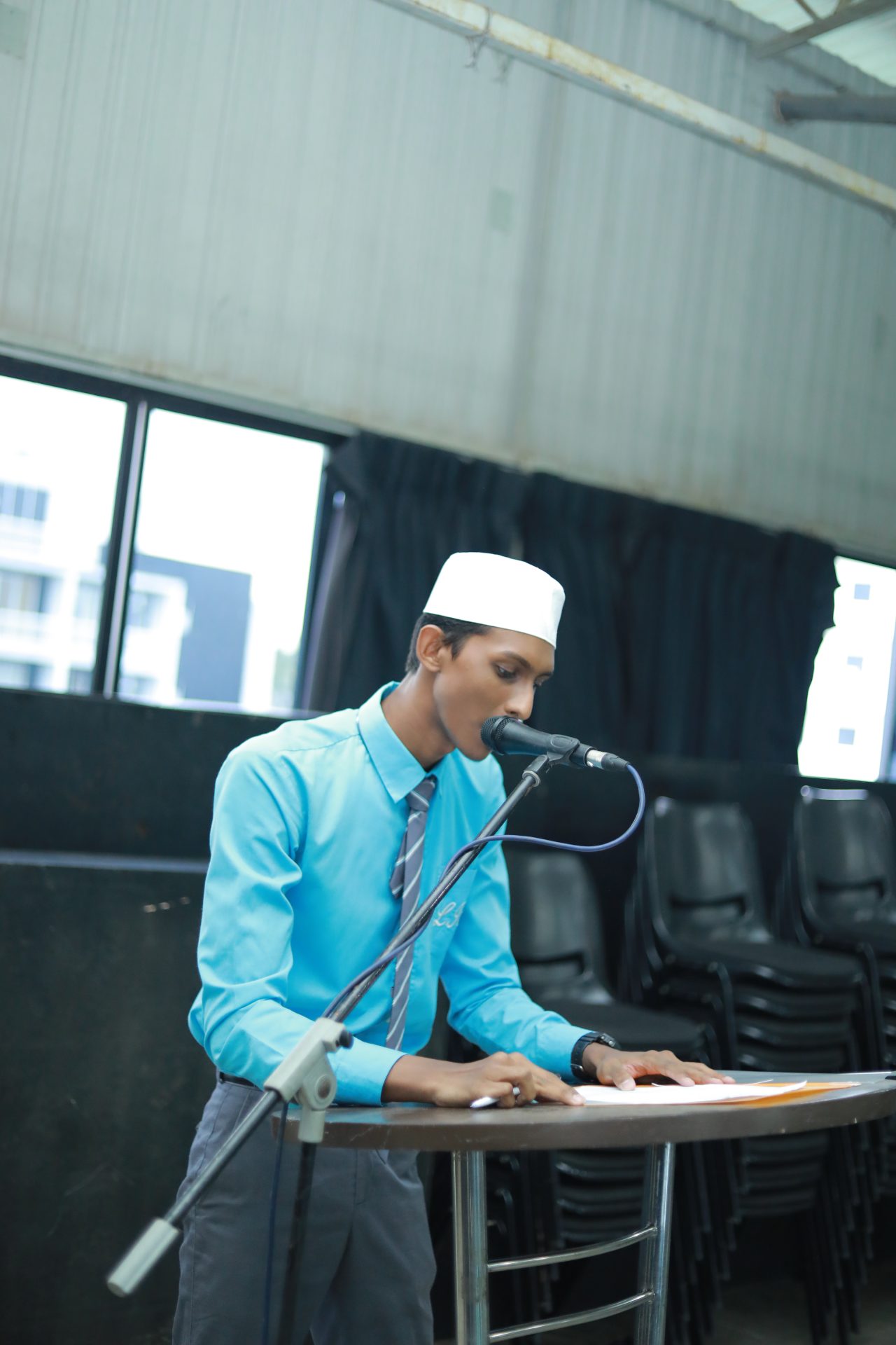 Formal presentation by a man in a blue shirt and white cap.
