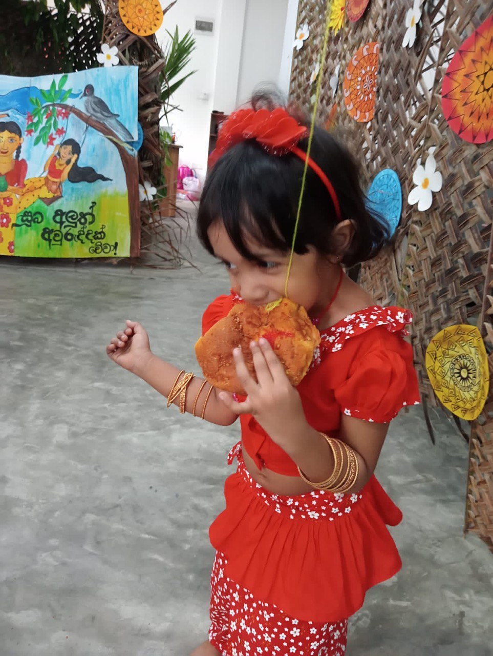 Young girl in red enjoying a festive treat amidst colorful cultural decorations.