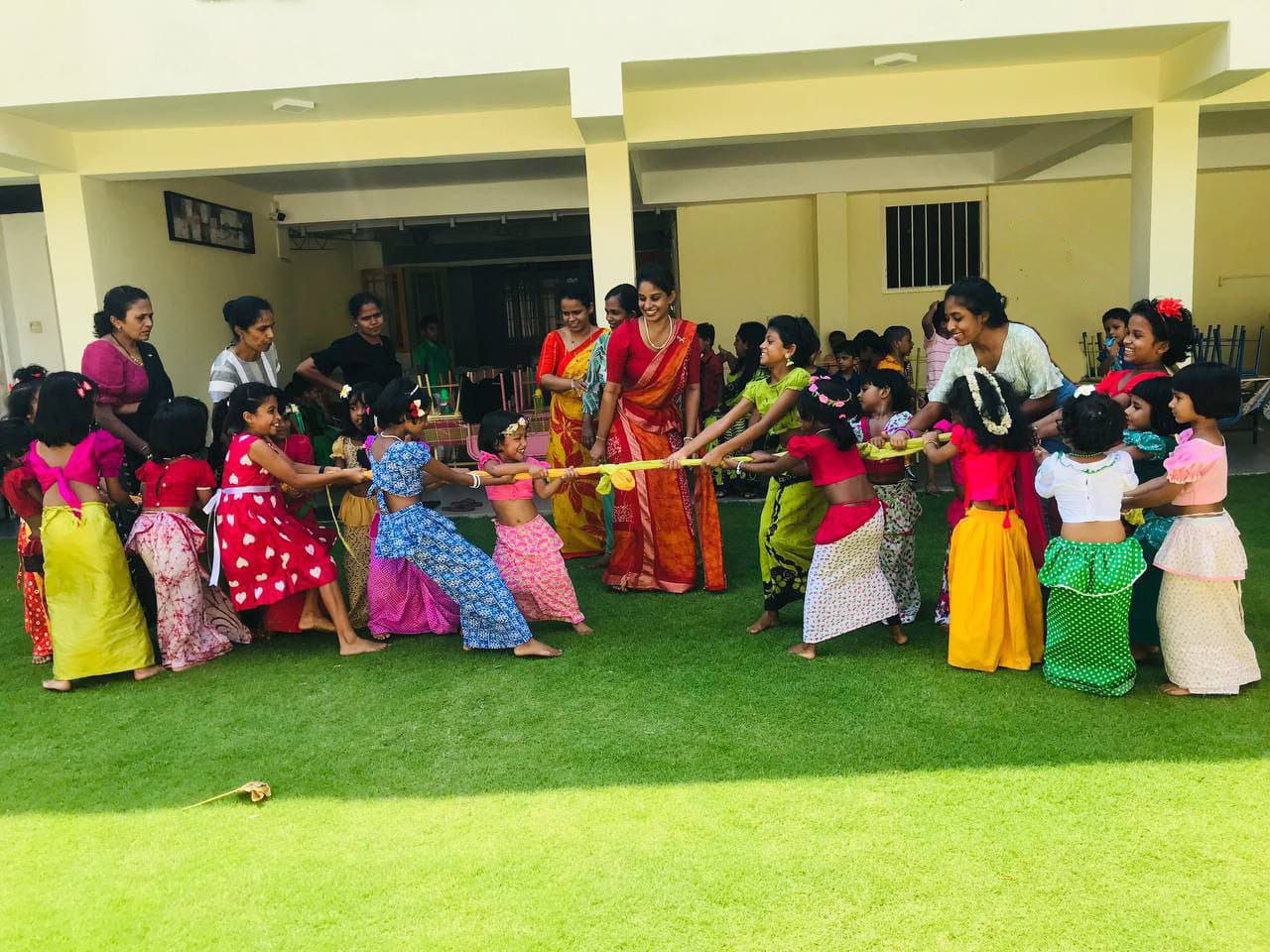 Children in colorful traditional attire playing tug-of-war at a cultural festival outdoors.