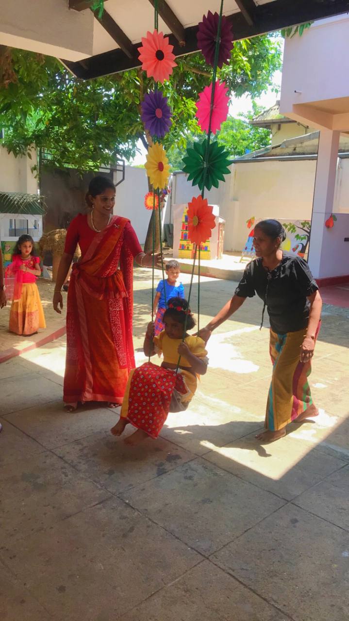 Child on a decorated swing in a festive, sunlit courtyard celebration.